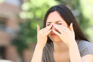 A woman with her eyes closed and her hands covering her nose and mouth, possibly in discomfort.