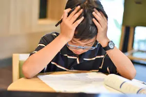 A boy sitting at a desk appears to be stressed about schoolwork.