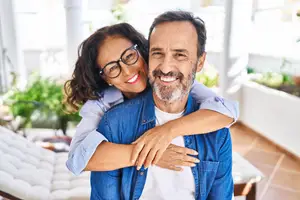 An elderly man and woman are smiling and hugging each other in a room.