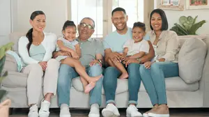 A family of five, including two young children, an elderly man, and two women, are sitting on a couch in a room, smiling and posing for a photo