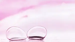 Two transparent contact lenses floating on a pink surface