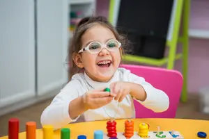 Young girl wearing glasses playing with a colorful educational toy on a table in a classroom