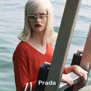 A woman with blonde hair wearing a red top and sunglasses is standing on a metal ladder by the water.