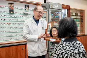 An optometrist is helping a customer with a pair of glasses in an optical shop