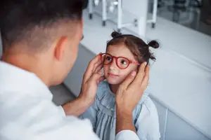 A man adjusting a young girl's glasses in a medical setting