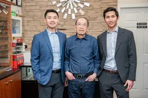 Three men in business suits standing in front of a brick wall with a clock and shelves