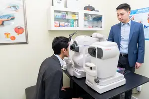 Two men in suits are in a medical office with a medical examination machine in front of them.