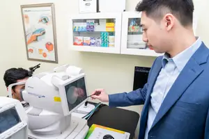 A man in a suit uses a medical device to test a patient's eye in a medical office