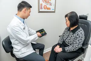 A doctor is showing a tablet to a patient in an office setting.