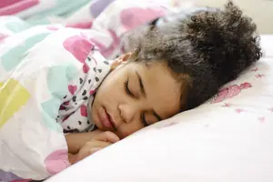 A young girl with curly hair is sleeping peacefully on a bed with colorful bedding.