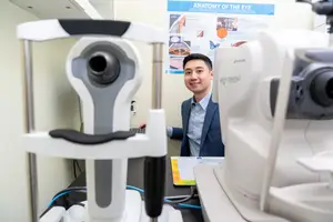 A man in a blue suit is standing next to an eye examination machine in an office.