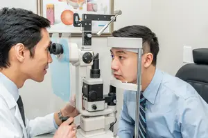 An optometrist checks a patient's eye using an ophthalmoscope in an exam room.