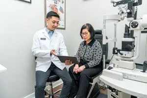 An ophthalmologist is discussing eye care with a patient in an office while looking at a tablet.