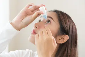 A woman is applying eye drops to her eye while looking down.