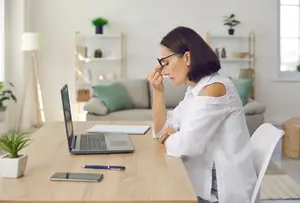 A woman sitting at a desk with a laptop, looking tired
