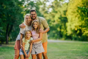 A family of four standing in a park with green grass and trees in the background