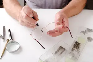 A man adjusts eyeglasses on a white table using a screwdriver and other tools.