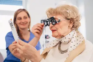 An elderly woman is getting her vision checked by a female optometrist in a clinic setting.
