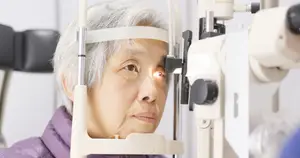 An elderly woman wearing a purple jacket is having her eye examined by an optometrist.