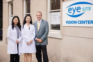 Three people, two women and a man, are standing in front of a building with the Eye Site Vision Center sign on it.