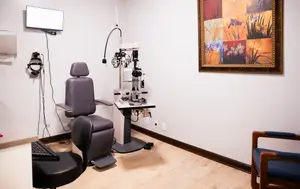 An optometrist's office with a monitor, an eye exam machine, and a framed picture on the wall.