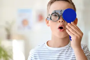 A boy wearing a blue magnifying glass on his forehead and looking surprised