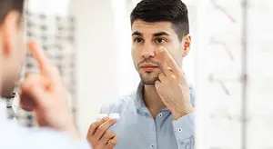 Man applying eye drops in front of a mirror