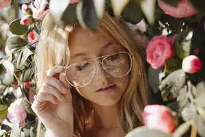 Blonde woman wearing sunglasses and standing in a garden of pink flowers