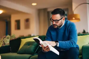 A man is sitting on a couch reading a book.