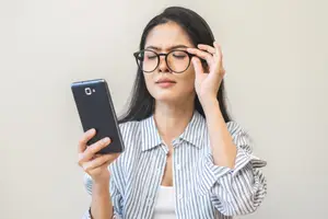 An adult woman squinting at a smartphone