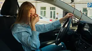 A woman sitting in a car is covering her eyes with her hand, possibly because she is crying or in pain.