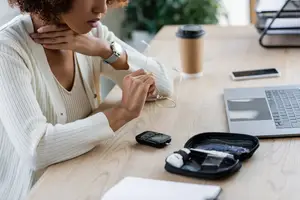 A woman is sitting at a desk, adjusting her glasses and looking at her laptop.