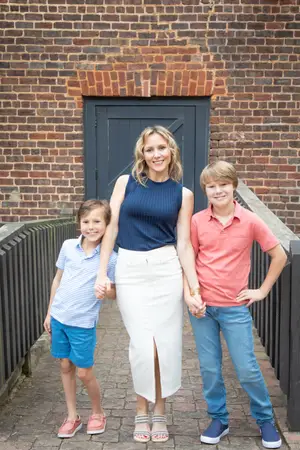 A woman and her two young sons are standing in front of a brick building and smiling for a photo.