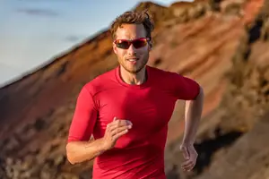 Man jogging on a mountain trail with rocks and mountains in the background