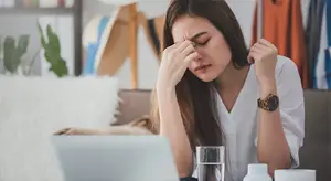Woman sitting at a desk with her hands covering her face, looking stressed or in pain
