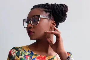 A woman with braided hair and glasses wearing a floral dress posing for a photo