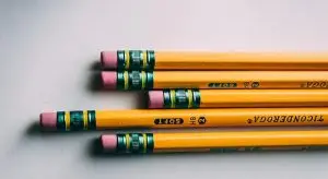 Five yellow pencils with green and pink erasers are neatly arranged on a white surface