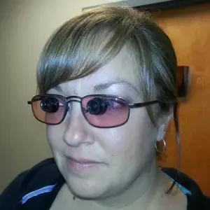 A woman with short hair wearing sunglasses with cameras on the lenses is smiling and posing for a photo