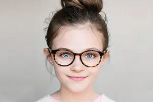 A girl with brown hair and glasses smiling at the camera