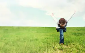 A child playing in a field with arms raised and looking up at the sky
