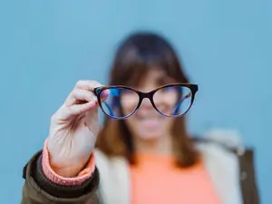 A woman holding up a pair of eyeglasses with a blue filter.