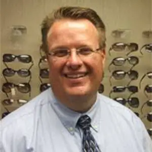 A man with glasses smiling in front of a display of sunglasses