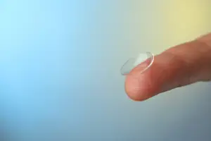 An image of a finger holding a contact lens in a blue and yellow background