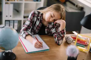 A girl is sleeping while holding a pen and a notebook on a desk
