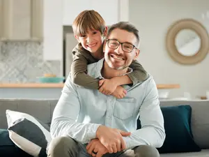 A father and his son sitting on a couch smiling at the camera