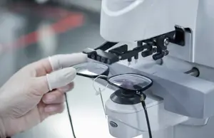 A person wearing gloves is adjusting a pair of eyeglasses on a machine