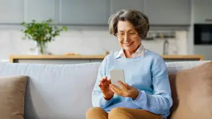 An elderly woman sitting on a couch holding a cell phone and smiling