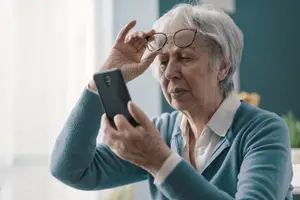 An elderly woman adjusting her glasses and looking at a smartphone
