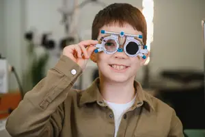 A boy wearing glasses with a white frame and a blue handle smiling at the camera.