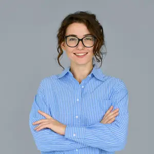 A woman in a blue striped shirt and glasses is smiling and posing for a photo with her arms crossed.